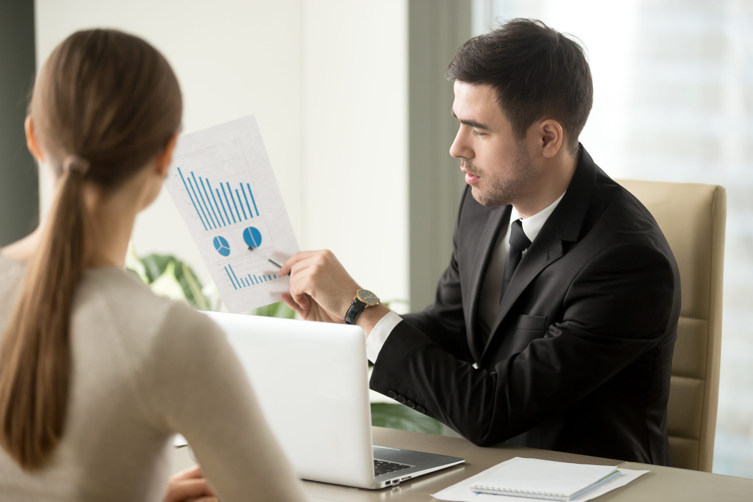 Male financial adviser showing document with profitability forecast to female client. Bank employee explaining terms of loan agreement and interest rate to borrower. Business plan presentation concept