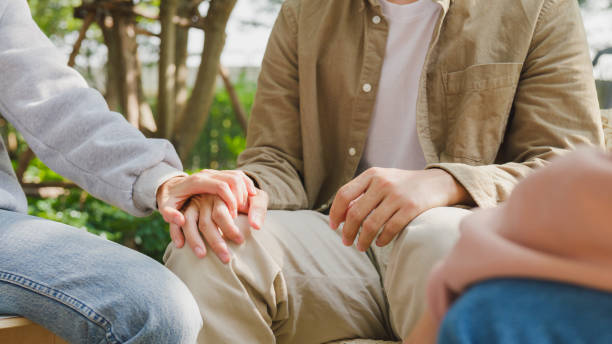 Close-up of diverse multiracial men and women group sit in circle hold hands together hope for help people in park. Support and understand at psychological therapy session, PTSD Mental health concept.