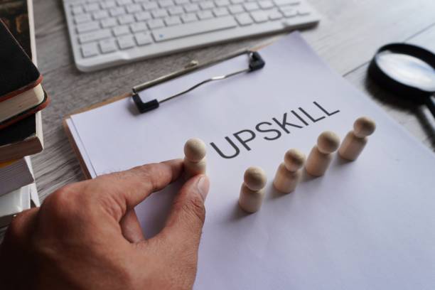 Closeup image of paper clipboard with text UPSKILL and wooden dolls on office office desk.