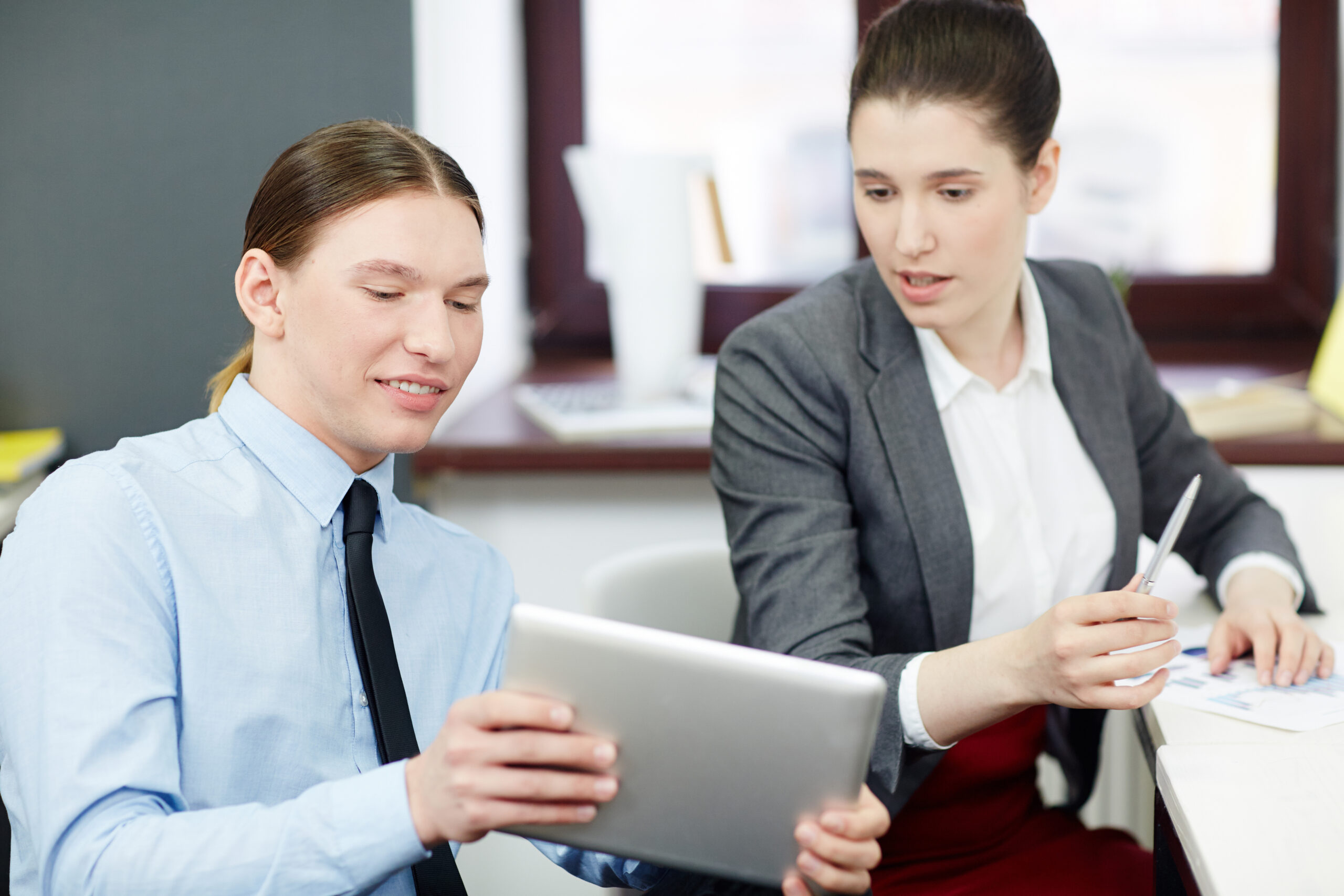 Working process in open plan office: young manager sharing ideas with his pretty colleague while having project discussion, he holding digital tablet in hands